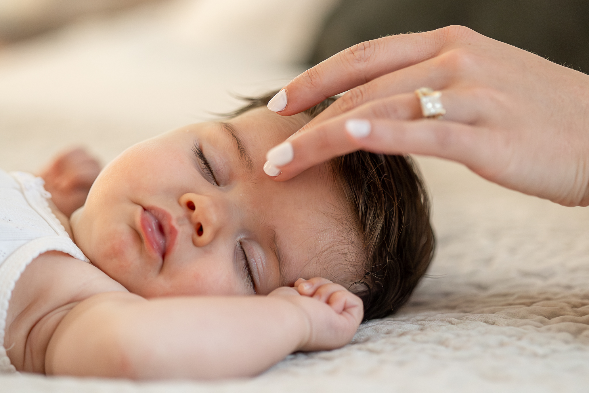 Sleeping newborn as a mother's hand gently brushes the baby's hair